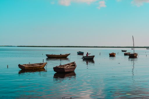 A wide shot of wooden small boats in the water with an African-American person in one of them