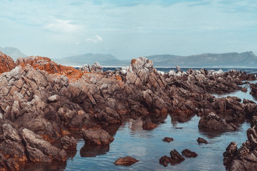 A landscape shot of big rocks in the seashore with a cloudy sky and mountains in the background