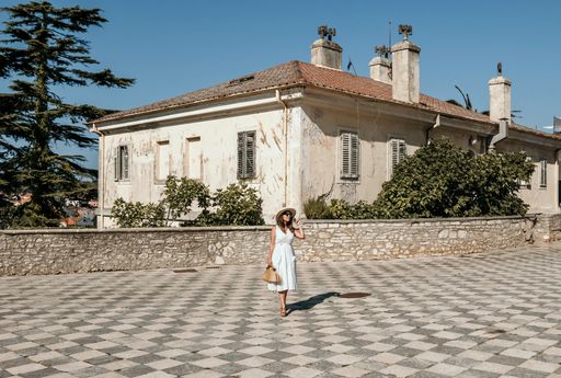 Full length portrait of young woman in white summer dress standing in middle of square in old town. Fashion, style, summer, travel, wanderlust.