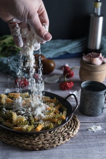 A cook's hand pouring flour in the fusilli pasta pot with fresh ingredients for cooking on a wooden rustic table