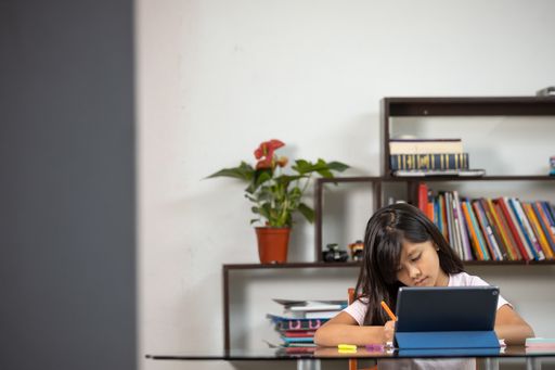 A pretty Hispanic schoolgirl writing concentrated on her notebook at home - online education