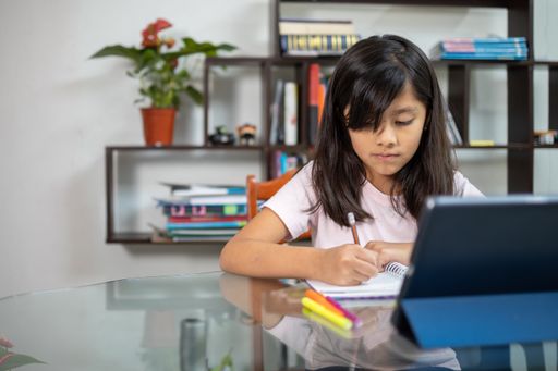 A pretty Hispanic schoolgirl writing concentrated on her notebook at home - online education