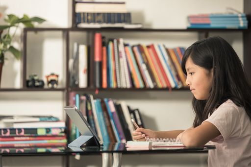 A Hispanic schoolgirl doing a homework using a notebook and tablet at home - online education