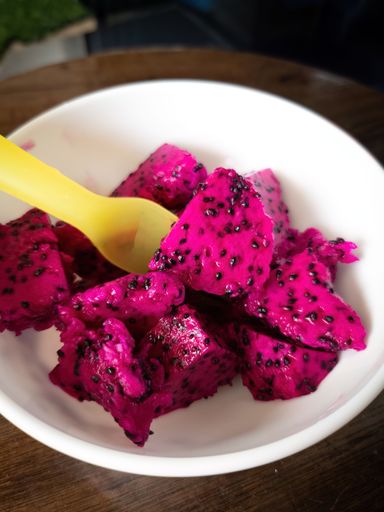 A vibrant yellow spoon resting in a white bowl filled with vivid, pink dragon fruit slices