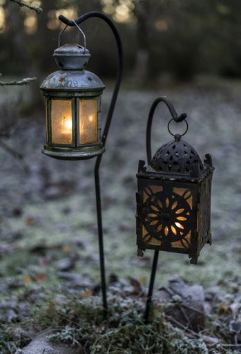 A closeup shot of two small lit vintage lanterns in the garden