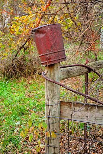 A vertical shot of a rusty red bucket on a wooden fence