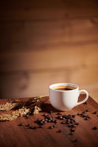A vertical shot of a cup of coffee and beans on a wooden table