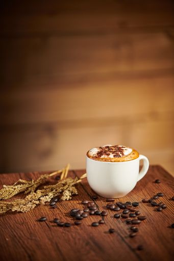 A vertical shot of a cup of coffee on a wooden table with scattered beans