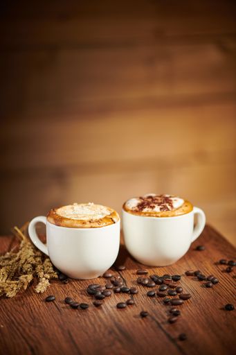 A vertical shot of cups of coffee on a wooden table with scattered