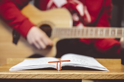 A person playing the guitar with note sheets on the table under the lights