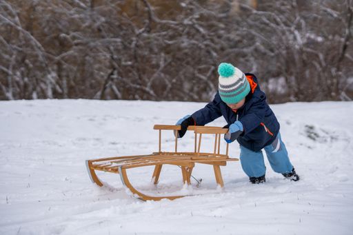 Young small boy and wooden sled on white snow at the park on a cold winter day