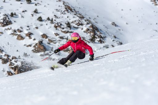 A young blonde woman in ski goggles and helmet skiing on a snowy mountain slope