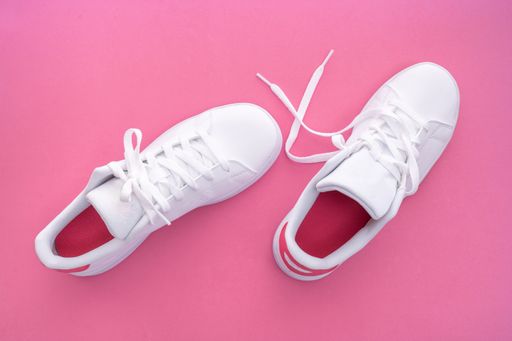 A top view of stylish round-toe white sneakers on the pink background