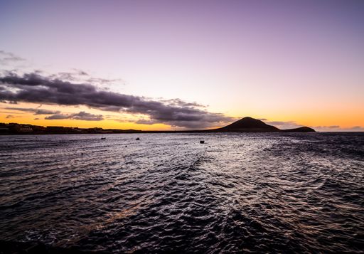 A wide shot of a sunrise in the ocean with a purple sky in the background