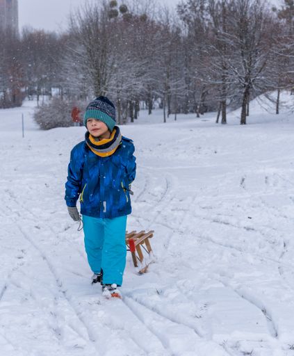 Young Polish Caucasian boy pulling a wooden sled on snow at a park on a cold winter day.