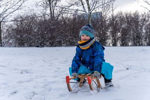 Young Polish Caucasian six years old boy sitting on wooden sled on a snow hill at a park on a cold winter day.