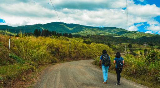 A two tourists walking on a road towards the big green hills