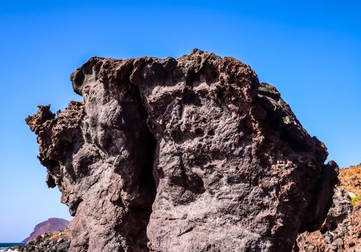 A low angle shot of a big rock on a beach with a clear blue sky in the background