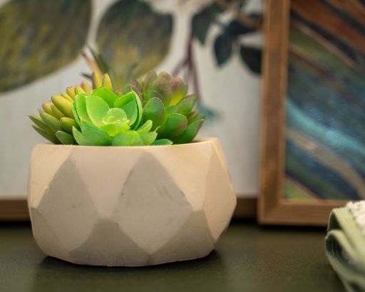 A modern wooden table with a potted plant and a framed artwork hung on the wall in the background