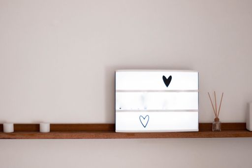 A white blank board with hearts on a wooden shelf with candles and aromatic reed diffuser