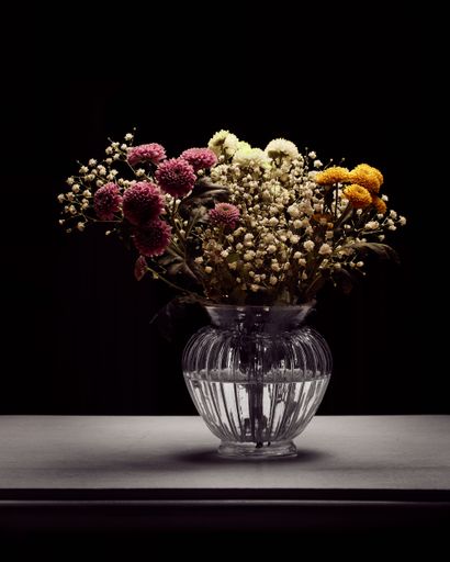 A transparent ceramic vase filled with various colorful flowers is prominently displayed on a wooden table