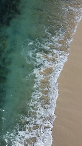An aerial view of Ocean waves crashing onto a sandy shoreline
