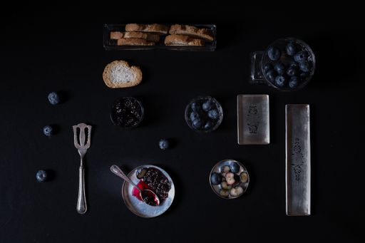 An aerial shot of berries and bread in small containers with black color in the background