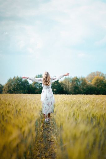 A young female in a long white dress walking in a field of wheat with wide-open arms enjoying the view