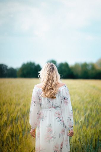 A young female in a long white dress walking in a field of wheat at daytime