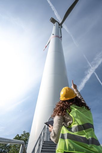 A female professional wearing a hard hat standing and pointing to a windmill