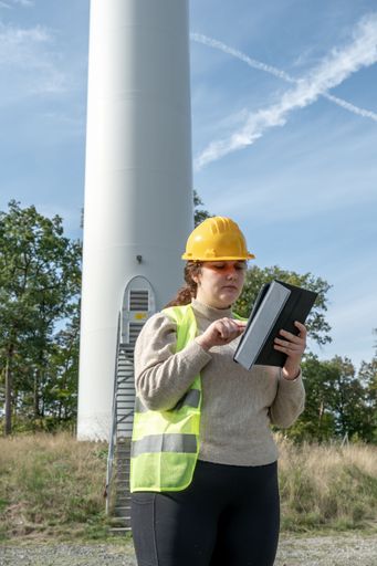 A female engineer in a safety hat is intently focused on her tablet