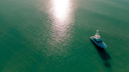 An aerial view of a small boat sailing in the green water in sunny weather