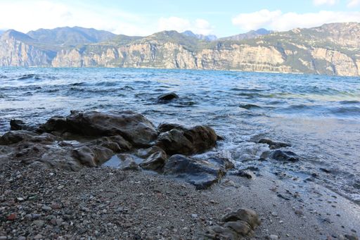 A landscape shot of big rocks in the seawater surrounded with mountains in a clear blue sky