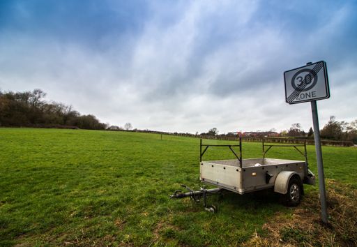 A landscape shot of a 30 zone ends road sign with white trailer cart with a clear white sky in the background