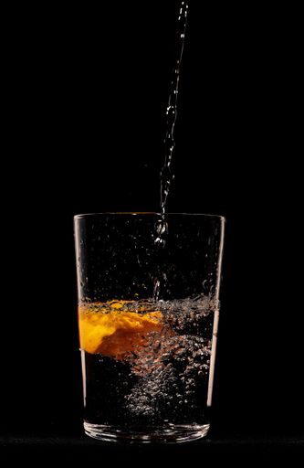 A vertical shot of water pouring into a glass with citrus