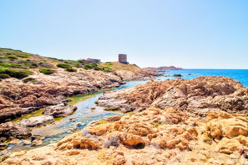 A landscape shot of rocky hills with castle building near the open sea with a clear sunny blue sky
