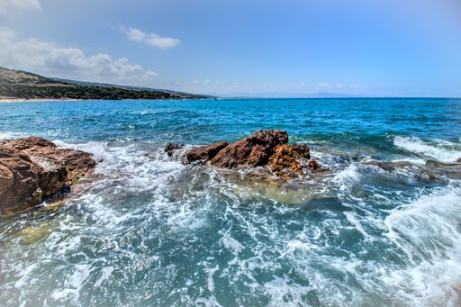 A landscape shot of green hills, big rocks in a blue ocean with clear blue sky