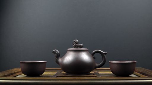 An ancient teapot and two clay bowls on a wooden surface with a grey background