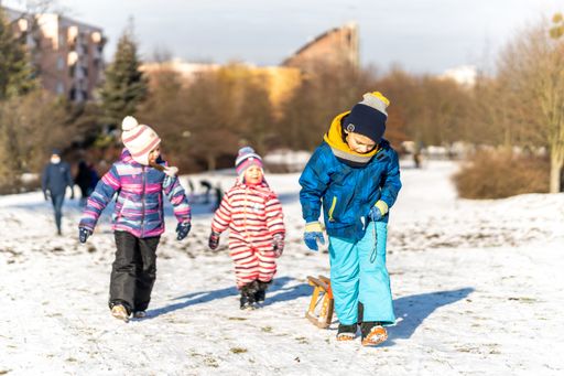 Young girls and boys walking on white snow and pulling wooden sleds at a park on a cold winter day.