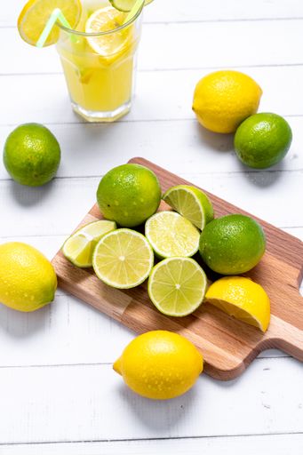 A vertical shot of lemon juice with straws, limes and lemons on the cutting board and on the table