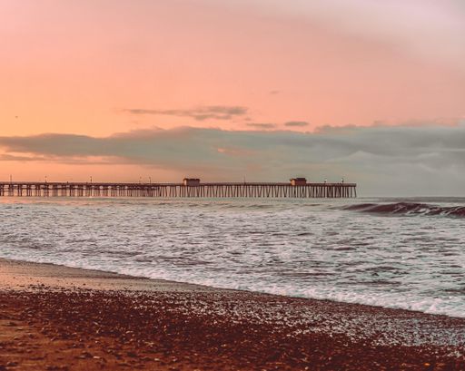 A  raised pier structure above a body of wavy seawater with a majestic sunset view beh