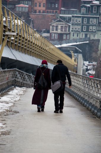A vertical shot of a male and a female walking through the bridge on a cold winter day