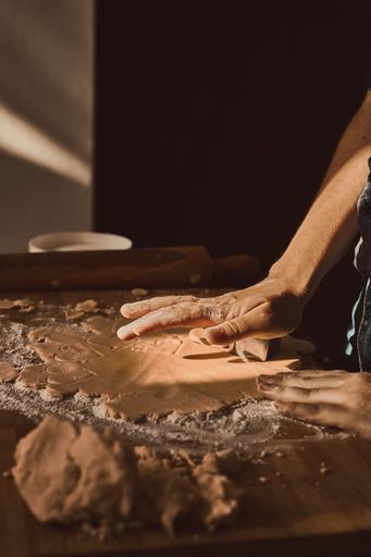 A woman's hand kneading the dough with a rolling pin on a wooden surface