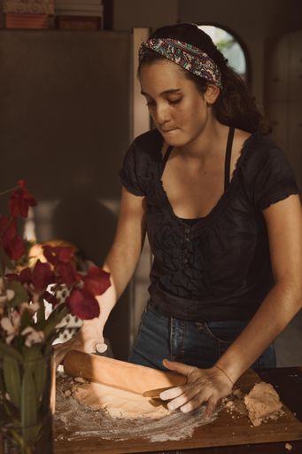 A Hispanic woman kneading the dough with a rolling pin on a wooden surface