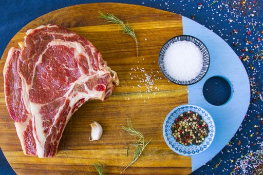 A slice of raw beef meat with spices and rosemary on a wooden board