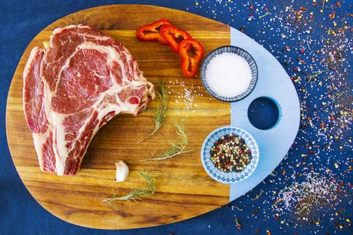 A top view of raw beef meat with spices and pepper on a wooden board