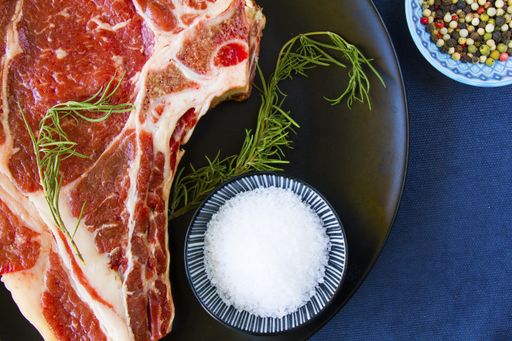 A slice of raw beef meat on the table with rosemary and other spices, Rib eye steak ingredients