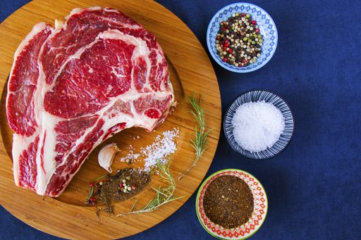 A slice of raw beef meat on the table with rosemary and other spices, Rib eye steak ingredients