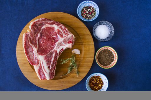 A slice of raw beef meat on the table with rosemary and other spices, Rib eye steak ingredients