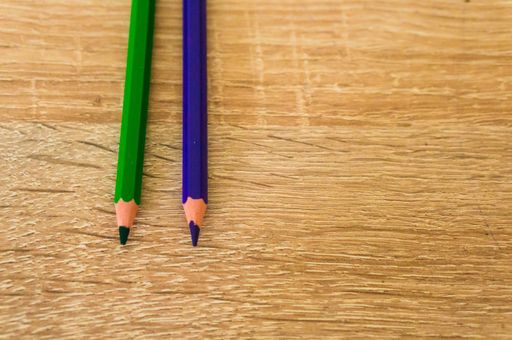 A high angle shot of two green and purple pencils on a wooden surface